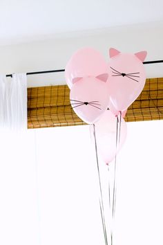 three pink balloons with cats on them in front of a window sill and curtain