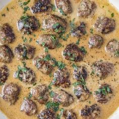 a white bowl filled with meatballs covered in gravy and garnished with parsley