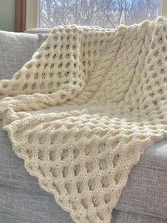 a white knitted blanket sitting on top of a couch in front of a window