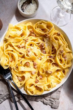 a white bowl filled with pasta and sauce next to two wine glasses on a table