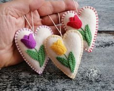 three felt heart ornaments with flowers on them hanging from strings in the palm of someone's hand