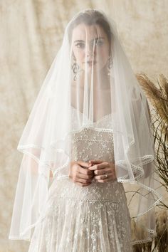 a woman in a wedding dress with a veil over her head and flowers behind her