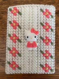 a hello kitty pin sitting on top of a white knitted object with flowers and leaves