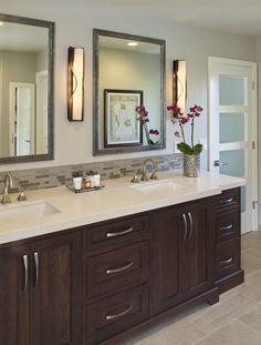 a bathroom with double sinks and two mirrors on the wall above them, along with vases filled with flowers