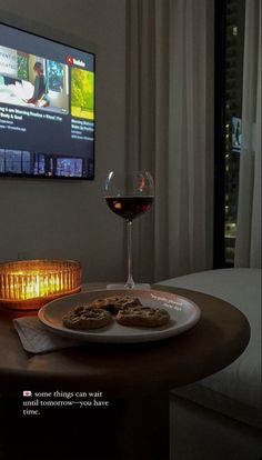 a glass of wine and some food on a table with a television in the background