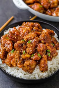 a black plate topped with meat and rice next to chopsticks on a table