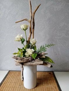 a white vase filled with flowers sitting on top of a wooden table next to a wall