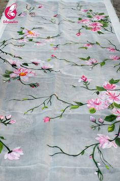 a white table cloth with pink flowers and green leaves on it, sitting on the ground