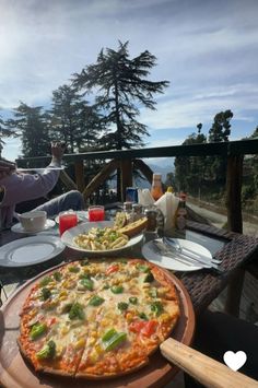 a pizza sitting on top of a wooden table next to plates of food and drinks