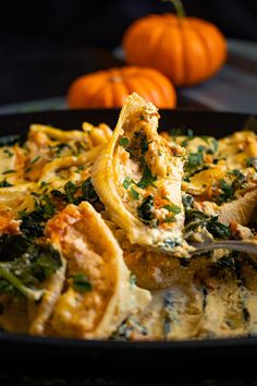 a pan filled with pasta and spinach on top of a table next to pumpkins