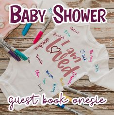 the baby shower guest book onesie is next to markers, pens and crayons