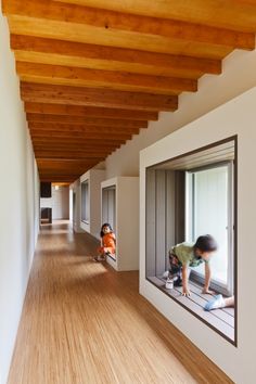 two children are playing on the floor in an empty room with wooden ceilings and white walls