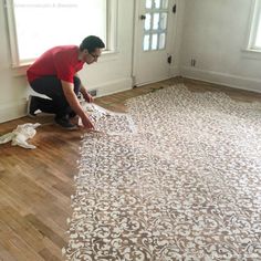 a man kneeling down on the floor to paint a large wallpapered area in a house