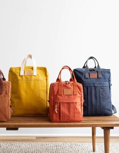 four different colored bags sitting on top of a wooden bench