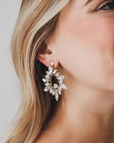 a woman with blonde hair wearing a pair of gold and crystal earrings, looking up at the sky