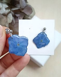 a pair of blue flower shaped earrings sitting on top of a white box next to a plant