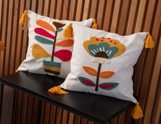 two decorative pillows with tassels sit on a black shelf next to a wooden wall