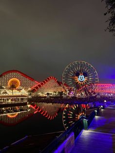 amusement park at night with ferris wheel and lights reflecting in the water, lit up by brightly colored lights