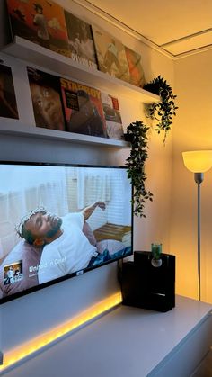 a flat screen tv sitting on top of a white table next to a plant and lamp