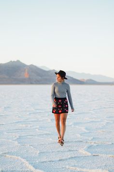 a woman walking across a salt flat with mountains in the backgrounnds