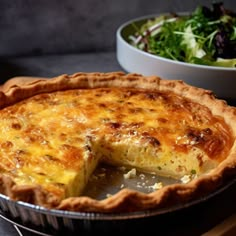 a quiche pie with a slice missing from it and a salad in the background