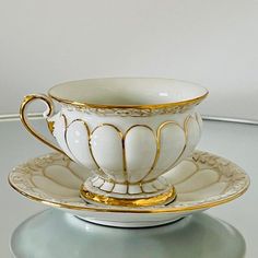 a white cup and saucer sitting on top of a glass table with gold trimmings