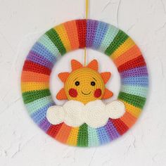 a crocheted wreath with a smiling sun and clouds hanging from the center, in front of a person's hand