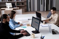 three people sitting at a table working on computers