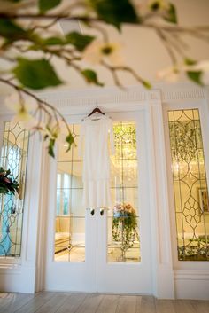 a white dress hanging on the front door to a house with glass doors and flowers