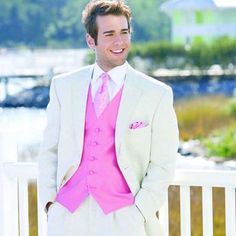 a man in a white suit and pink tie standing on a porch next to water