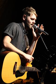 a man singing into a microphone while holding an acoustic guitar in front of his face