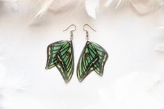 a pair of earrings with green and black designs on them, sitting on white feathers