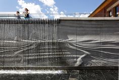 two women are standing on the edge of a wall with water running down it and behind them is a waterfall