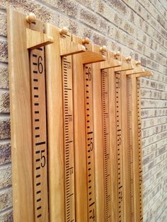 four wooden rulers are lined up against a brick wall, with one measuring the length