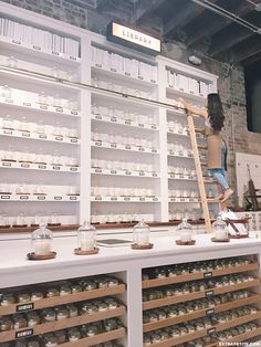 a woman standing on top of a ladder in front of shelves filled with jars