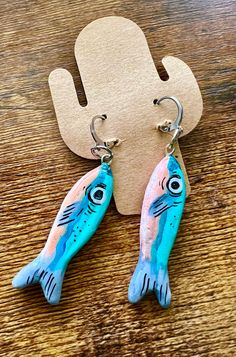 two fish shaped earrings sitting on top of a wooden table