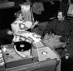 black and white photograph of two people sitting in chairs with record player on the floor