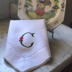 a white napkin with a green embroidered letter c on it