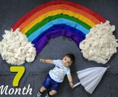 a baby laying on the ground next to a rainbow made out of yarn