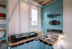 a kitchen with blue walls and wooden shelves next to a stove top oven in a small room