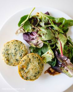 a white plate topped with spinach and two small patties next to a salad