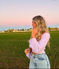 a woman is standing in the middle of a field talking on her cell phone and looking off into the distance