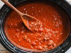 a wooden spoon in a slow cooker filled with chili sauce and meatballs, ready to be cooked