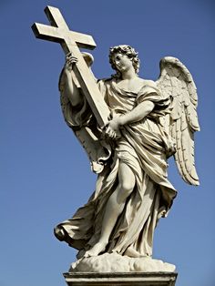 an angel statue holding a cross on top of a rock