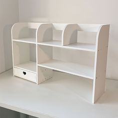 a white shelf with two open shelves on top and one closed drawer below it, in front of a wall