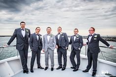 a group of men standing on top of a boat next to each other in suits