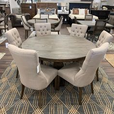 a dining room table surrounded by chairs and rugs in a furniture store with lots of couches