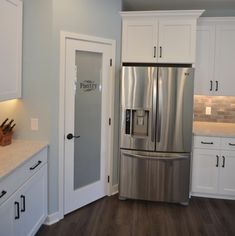 a stainless steel refrigerator in a kitchen with white cabinets and wood flooring on the walls