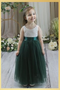 Hunter Green Flower Girl Dress in Sleeveless Fairytales do come true in our full length lace back dress in hunter green. This classic design is so sweet, featuring a low back lace bodice with scalloped edges and a layered tulle skirt that is extra full and dreamy. Ideal for that pretty flower girl dress, birthday party dress or special occasion. Dress Features A soft white bodice, made of stretchy lace with a "V" shaped on the back, edged with delicate lace A cotton liner under 2 layers of soft tulle that won’t itch your princess. Dress length of mid-calf to floor depending on child’s height Sashes are not attached and come in a variety of options from a plain sash, jewels/rhinestones and flowers Large Floral Sash comes in Navy, ivory, creams, and white flowers. Attached to a navy sash. Th Green Boho Flower Girl Dresses, Hunter Green Flower Girl Dress, Green And Black Flower Girl Dress, Hunter Green Toddler Dress, Emerald Flower Girl Dress, Green Flower Girl Dress, Lace Back Dress, Green Flower Girl Dresses, Dress Birthday Party