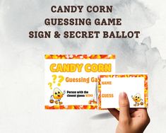 a hand holding up a candy corn sign and secret ball game card with question marks on it